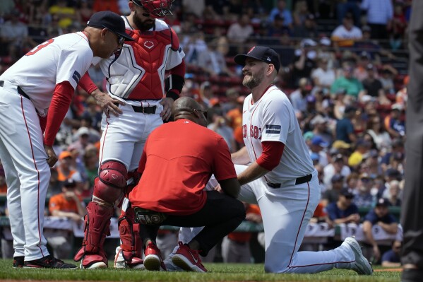 Boston Red Sox manager Alex Cora, left, and a trainer check on starting pitcher James Paxton, right, during the first inning of a baseball game against the Houston Astros, Sunday, Aug. 11, 2024, in Boston. (AP Photo/Michael Dwyer)