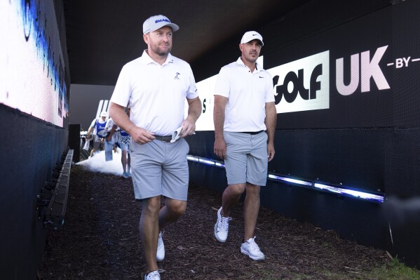 Graeme McDowell of Smash GC and Captain Brooks Koepka of Smash GC walk to the 14th hole during the first round of LIV Golf United Kingdom by JCB at JCB Golf & Country Club on Friday, July 26, 2024, in Rocester, England. (Photo by Chris Trotman/LIV Golf via AP)