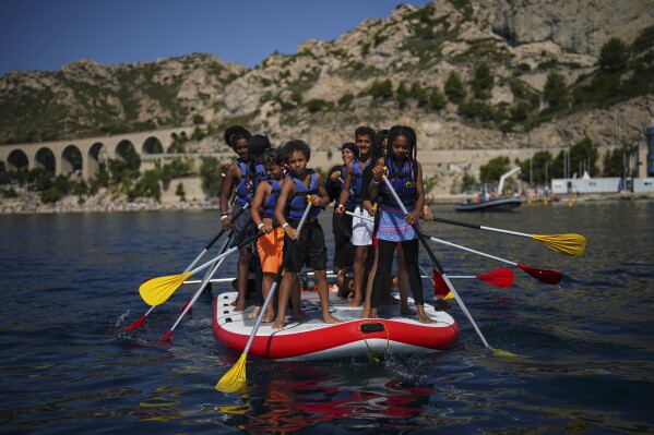 Children attend a swimming camp organized by the Grand Bleu Association which facilitates access to the sea for marginalized children in Marseille, France, Friday, July 26, 2024. Marseille, a millennia-old port, is a crossroads of cultures and faiths, where the sea is ever present but not equally accessible, and the beauty and cosmopolitan flair rub shoulders with enclaves of poverty and exclusion even more intimately than in the rest of France. (AP Photo/Daniel Cole)