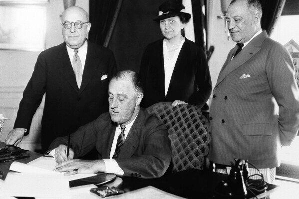 FILE - President Franklin D. Roosevelt signs the Wagner Unemployment Bill at the White House in Washington, June 6, 1933. Standing behind him, from left, are: Rep. Theodore A. Peyser, D-N.Y., Labor Secretary Frances Perkins, and Sen. Robert Wagner, D-N.Y. (AP Photo, File)