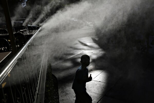 FILE - A child keeps cool beneath misters along the Las Vegas Strip, Friday, June 16, 2017, in Las Vegas. Pediatricians suggest keeping your child hydrated and avoiding prolonged sun exposure to keep heat illness at bay. (AP Photo/John Locher, File)