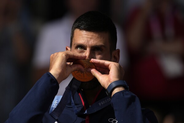 Serbia's Novak Djokovic kisses his gold medal after defeating Spain's Carlos Alcaraz during the men's singles tennis final at the Roland Garros stadium during the 2024 Summer Olympics, Sunday, Aug. 4, 2024, in Paris, France. Djokovic has won his first Olympic gold medal by beating Alcaraz 7-6 (3), 7-6 (2) in the 2024 Games men's tennis singles final. (AP Photo/Louise Delmotte)