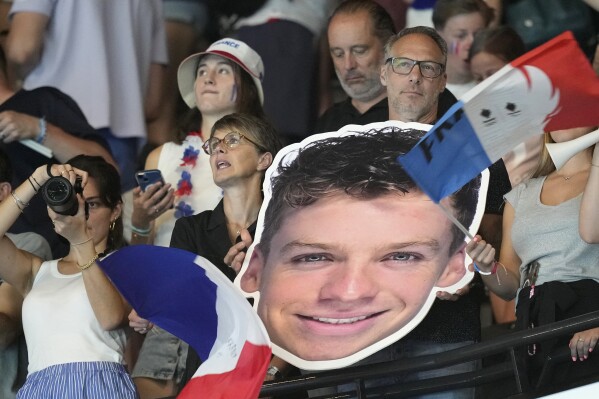 Fans hold placards featuring Leon Marchand of France, following his men's 200-meter individual medley final win at the 2024 Summer Olympics, Friday, Aug. 2, 2024, in Nanterre, France. (AP Photo/Tsvangirayi Mukwazhi)