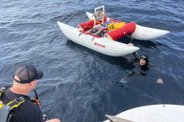 In this image provided by Jonathan Boeve, Jim Dreyer, right, talks to his support team in Lake Michigan, Thursday, Aug. 8, 2024, on the third day of his attempt to swim from Michigan to Wisconsin. (Jonathan Boeve via AP)