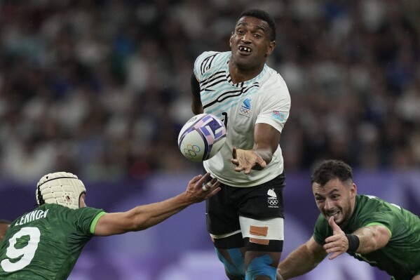 Fiji's Joji Nasova passes the ball as Ireland's Hugo Lennox, left tackles during the men's quarterfinal match Rugby Sevens between Fiji and Ireland at the 2024 Summer Olympics, in the Stade de France, Thursday, July 25, 2024, in Saint-Denis, France. (AP Photo/Tsvangirayi Mukwazhi)