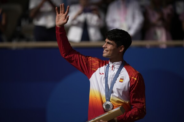 Spain's Carlos Alcaraz waves while wearing his silver medal after losing to Serbia's Novak Djokovic in the men's singles tennis final at the Roland Garros stadium during the 2024 Summer Olympics, Sunday, Aug. 4, 2024, in Paris, France. Djokovic has won his first Olympic gold medal by beating Alcaraz 7-6 (3), 7-6 (2) in the 2024 Games men's tennis singles final. (AP Photo/Louise Delmotte)