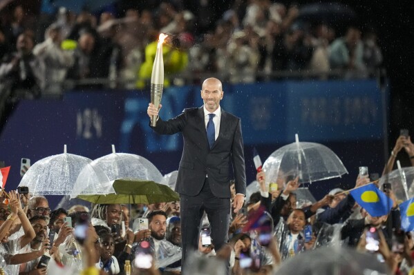 Zinedine Zidane carries the Olympic torch in Paris, France, during the opening ceremony of the 2024 Summer Olympics, Friday, July 26, 2024. (AP Photo/Thibault Camus)