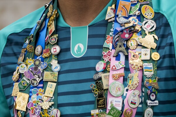 Olympic pins are worn by a volunteer in Paris, France, prior to the start of the opening ceremony of the 2024 Summer Olympics, Friday, July 26, 2024. (AP Photo/Andy Wong)