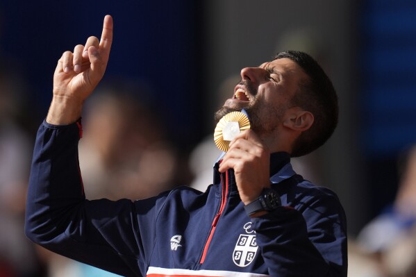 Serbia's Novak Djokovic shows his gold medal after defeating Spain's Carlos Alcaraz in the men's singles tennis final at the Roland Garros stadium during the 2024 Summer Olympics, Sunday, Aug. 4, 2024, in Paris, France. Djokovic has won his first Olympic gold medal by beating Alcaraz 7-6 (3), 7-6 (2) in the 2024 Games men's tennis singles final. (AP Photo/Manu Fernandez)