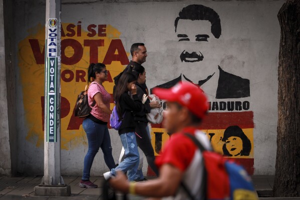 Pedestrians walk past a campaign mural featuring President Nicolas Maduro, in Caracas, Venezuela, Friday, Aug. 2, 2024. (AP Photo/Bernardo Suarez)