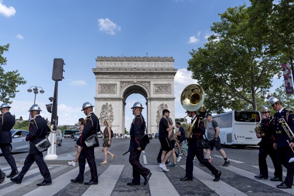 Members of a firefighter brigade band cross the street to perform at a ceremony at the Arc de Triomphe ahead of the 2024 Summer Olympics, Saturday, July 20, 2024, in Paris. (AP Photo/David Goldman)