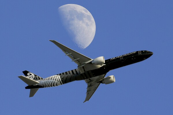 FILE - An Air New Zealand passenger plane flies past the moon on its way to the Los Angeles International Airport from London, in Whittier, Calif., Aug. 23, 2015. Air New Zealand scrapped its 2030 carbon emissions reduction targets on Tuesday, July 20, 2024, citing lags in producing new planes, a lack of alternative fuel and "challenging" regulatory and policy settings. (AP Photo/Nick Ut, File)