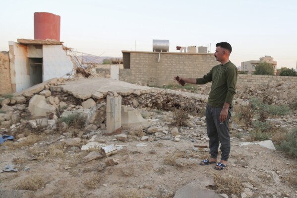 Hadi Shammo, 30, a Yazidi returnee, stands amid the wreckage of his destroyed family house in the village of Dugure in Sinjar, Iraq, Tuesday, July 16, 2024. "In the end we have to return here — our life is here" in Sinjar, said Shammo, whose family returned from a camp in Duhok area. "This is part of our identity." (AP Photo/Farid Abdulwahed)