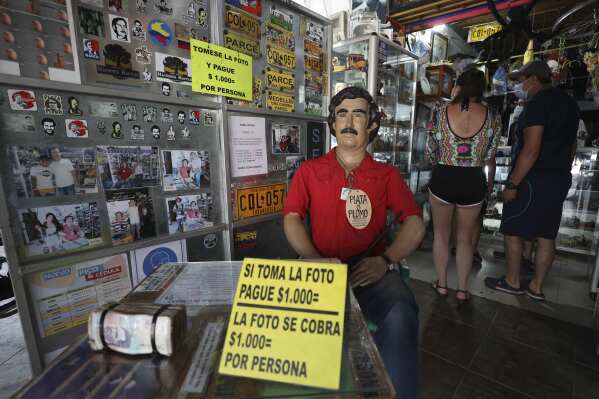 FILE - Tourists buy souvenirs of the late drug lord Pablo Escobar, featured as a statue with a sign that says one will be charged for taking photos inside a store in Doradal, Colombia, Feb. 5, 2021. Souvenirs depicting the Escobar could be banned in Colombia if legislators approve a bill introduced the week of Aug. 5, 2024. (AP Photo/Fernando Vergara, File)