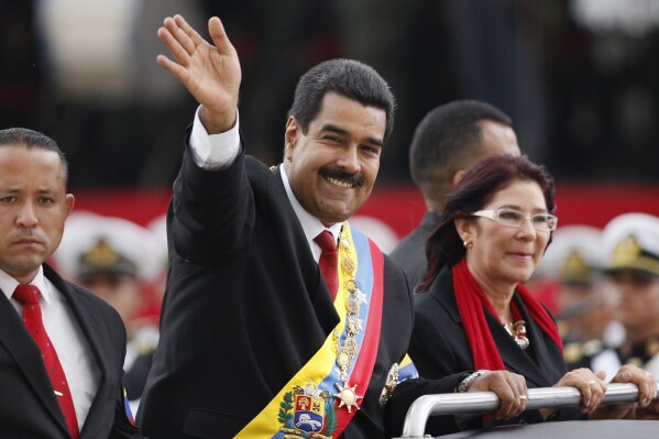 FILE - Venezuela's President Nicolas Maduro waves from a vehicle next to his companion Cilia Flores during a military ceremony recognizing him as commander-in-chief, in Caracas, Venezuela, April 19, 2013. (AP Photo/Ariana Cubillos, File)