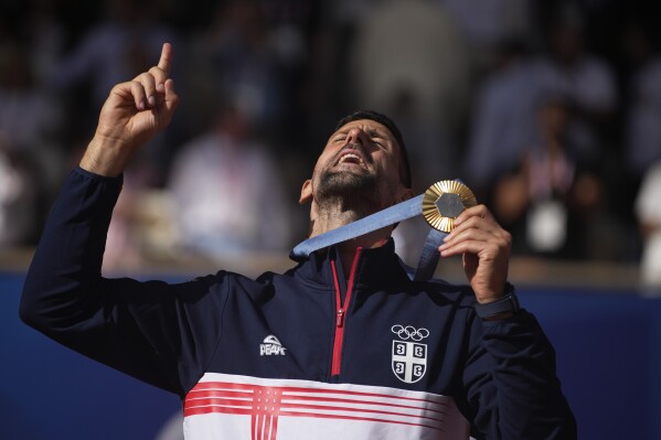 Serbia's Novak Djokovic shows his gold medal after defeating Spain's Carlos Alcaraz in the men's singles tennis final at the Roland Garros stadium during the 2024 Summer Olympics, Sunday, Aug. 4, 2024, in Paris, France. Djokovic has won his first Olympic gold medal by beating Alcaraz 7-6 (3), 7-6 (2) in the 2024 Games men's tennis singles final. (AP Photo/Louise Delmotte)