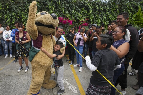 Wisin the “puppy luchador,” is embraced by a child as he greets fans at a lucha libre event at the Institute of Youth, in Mexico City, Thursday, July 25, 2024. Wisin was originally created by the institute to motivate children to exercise but his character evolved into a viral meme across Instagram, TikTok, and Twitter. (AP Photo/Fernando Llano)