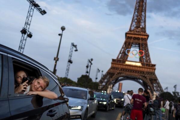 Passengers in the back of a taxi film themselves as they leave the Eiffel Tower decorated with the Olympic rings ahead of the 2024 Summer Olympics, in Paris, July 17, 2024. (AP Photo/David Goldman)