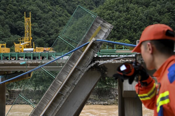 In this photo released by Xinhua News Agency, a rescuer looks at the collapsed bridge as they conduct a search and rescue on a river in Zhashui County in Shangluo City, northwest China's Shaanxi Province, Saturday, July 20, 2024. Chinese authorities say several people have died and more than dozen are missing in the partial collapse of a highway bridge in the northwest of the country following heavy storms and flooding. A similar number are missing in the southwest after dozens of houses were destroyed by storms. (Zou Jingyi/Xinhua via AP)