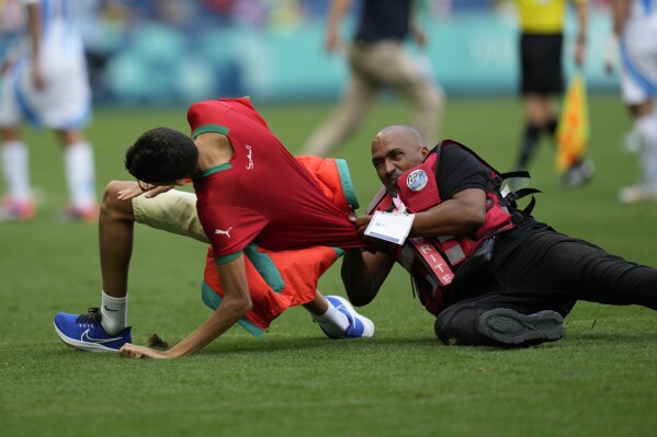 A steward catches a pitch invader during the men's Group B soccer match between Argentina and Morocco at Geoffroy-Guichard Stadium at the 2024 Summer Olympics, Wednesday, July 24, 2024, in Saint-Etienne, France. (AP Photo/Silvia Izquierdo)