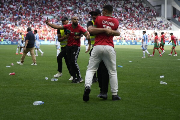 Stewards catch pitch invaders during the men's Group B soccer match between Argentina and Morocco at Geoffroy-Guichard Stadium at the 2024 Summer Olympics, Wednesday, July 24, 2024, in Saint-Etienne, France. (AP Photo/Silvia Izquierdo)