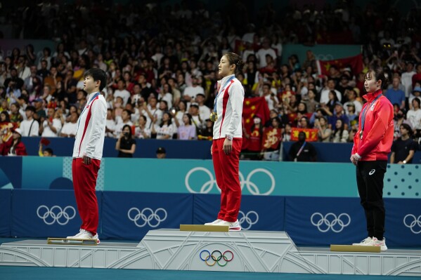 Gold medalist China's Chen Meng, center, silver medalist China's Sun Yingsha, left, and bronze medalist Japan's Hina Hayata stand for the Chinese national anthem during the medal ceremony of the women's singles table tennis at the 2024 Summer Olympics, Saturday, Aug. 3, 2024, in Paris, France. (AP Photo/Petros Giannakouris)