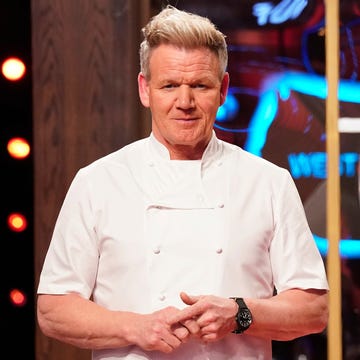 gordon ramsay stands in his chef jacket and looks at the camera, he hands are clasped in front of him