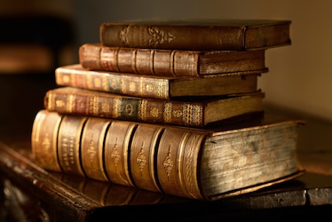 Vintage, antiquarian books pile on wooden surface in warm directional light.