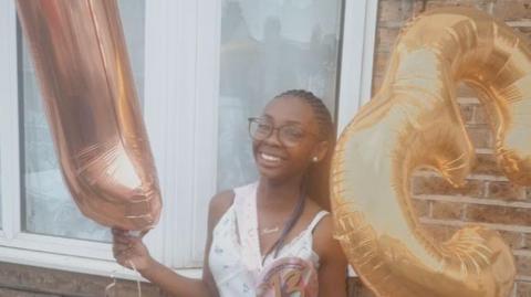 A smiling Hannah Jacobs poses with birthday balloons 