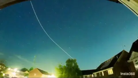 A meteor trail creates a white streak in the night sky above a row of houses