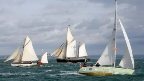 Three sailing boats out on the sea with people on board trying to move their vessels through the water