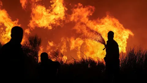 Silhouettes of firefighters are seen against a fiery backdrop of flames as wildfires rage in Dionysos, Greece, August 12, 2024.