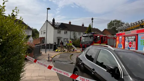 Firefighters outside an end terrace with burnt-out roof