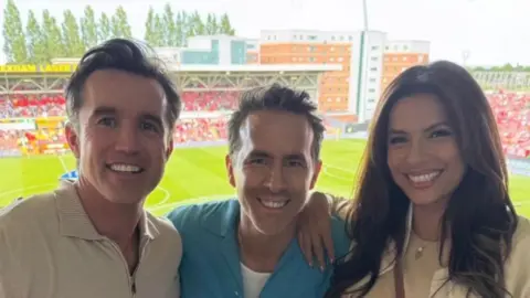 Eva Longoria with co-owners Rob McElhenney and Ryan Reynolds with the Racecourse ground in the background