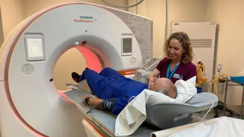 Man lying down about to enter a CT scanner with a nurse next to him