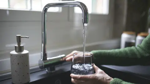 A person turning on a tap to fill a glass with water