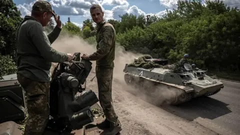 Ukrainian personnel look on as a Ukrainian tank passes by near the Russian border in the Sumy region