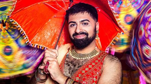 Vinay, a gender non-conforming Bollywood dancer - standing with multicoloured umbrellas twirling behind them.