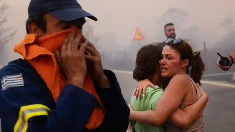 Women embrace after being rescued during a wildfire in Varnavas, north of Athens