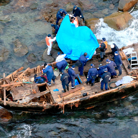 Police officers investigate a wooden boat marked with Hangul characters on Sado island, Niigata prefecture