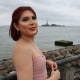 Michelle Carranza smiles outside, the statue of Liberty can be seen across the water in the distance