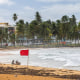 Tourists sit on the beach near a red flag.