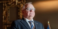 Tim Walz stands for a portrait, hands clasped and looking upwards