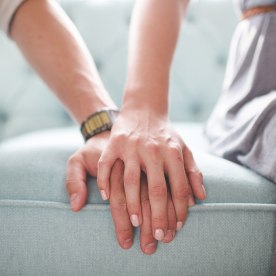 Waist photo of man and woman holding hands while sitting on a couch.